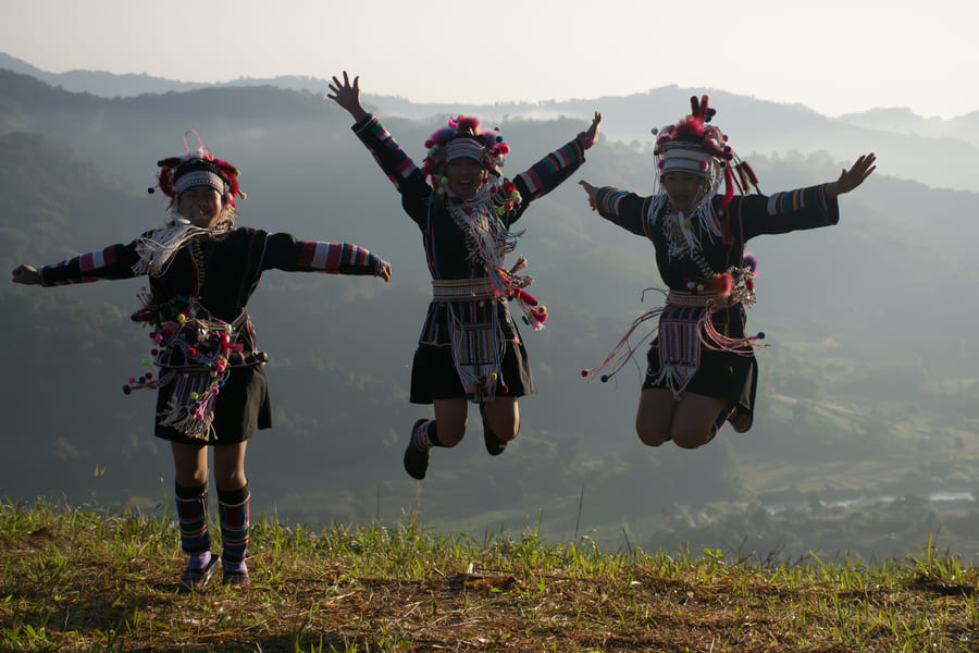 tres personas con traje típico de China, dando un salto de fondo las montañas