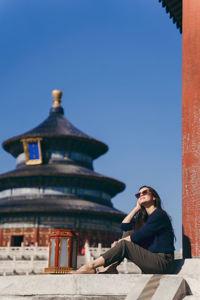 mujer sentada con lentes de sol frente a un monumento en beijing